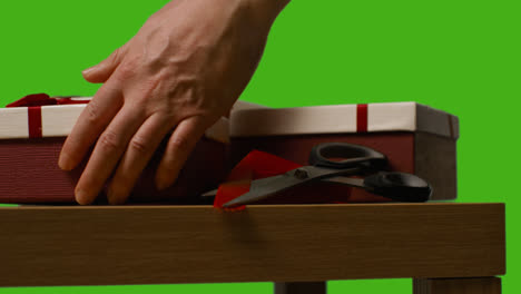 Close-Up-Of-Man-Gift-Wrapping-Presents-In-Boxes-Decorated-With-Ribbon-On-Table-Shot-Against-Green-Screen-1